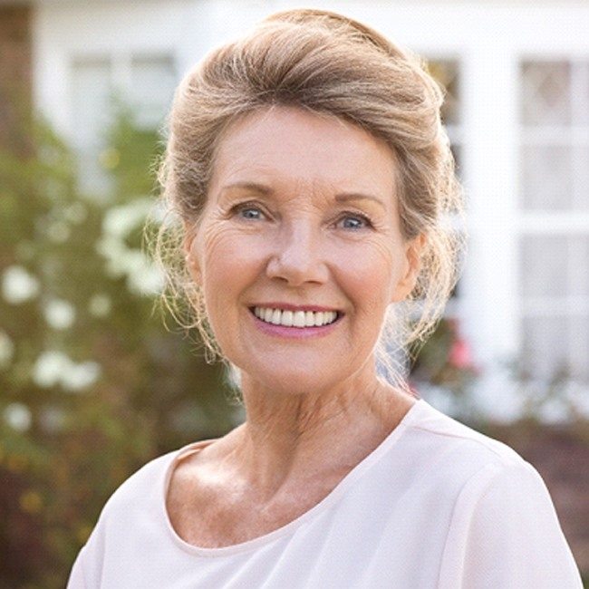 An older woman with dentures smiling outside.