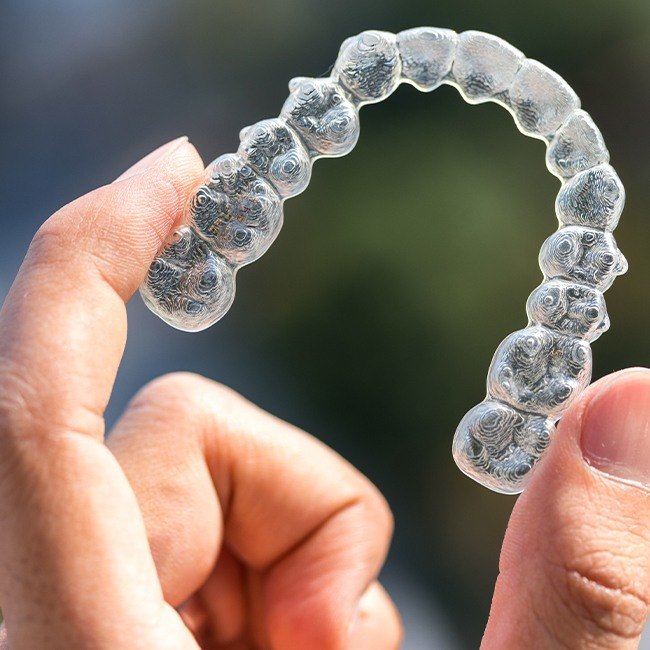 Hand holding an Invisalign® clear braces tray